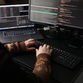 a person sitting at a desk with a laptop and a computer monitor