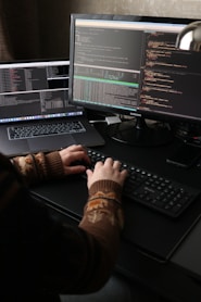 a person sitting at a desk with a laptop and a computer monitor