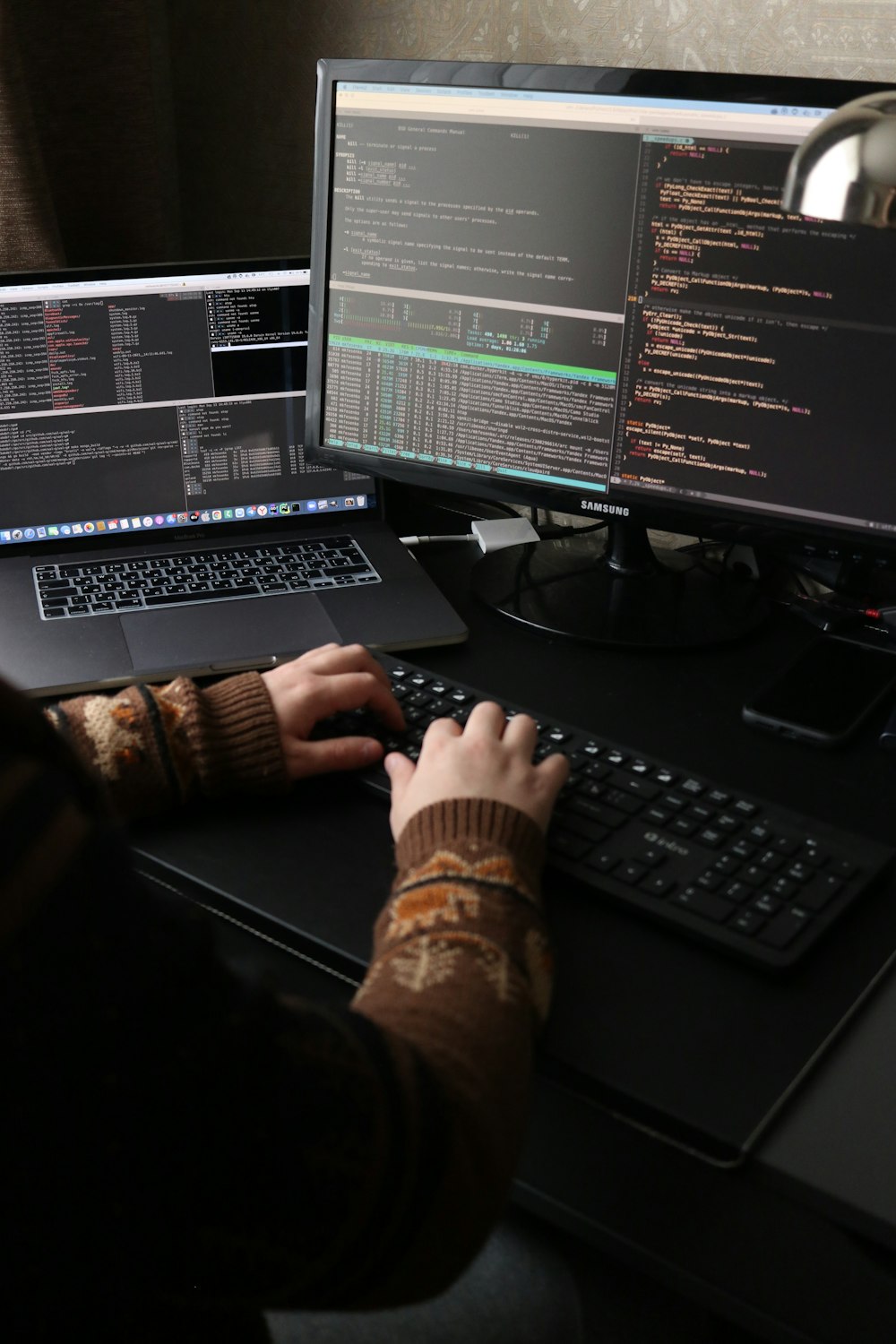 une personne assise à un bureau avec un ordinateur portable et un écran d’ordinateur