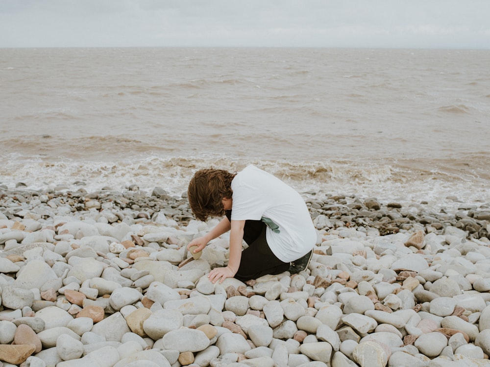 a person kneeling down on a rocky beach