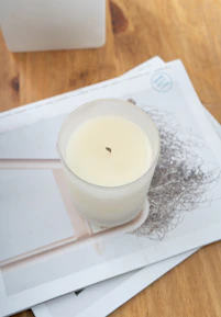 Close-up of a beautifully crafted candle beside a stack of educational magazines on a soft neutral background.