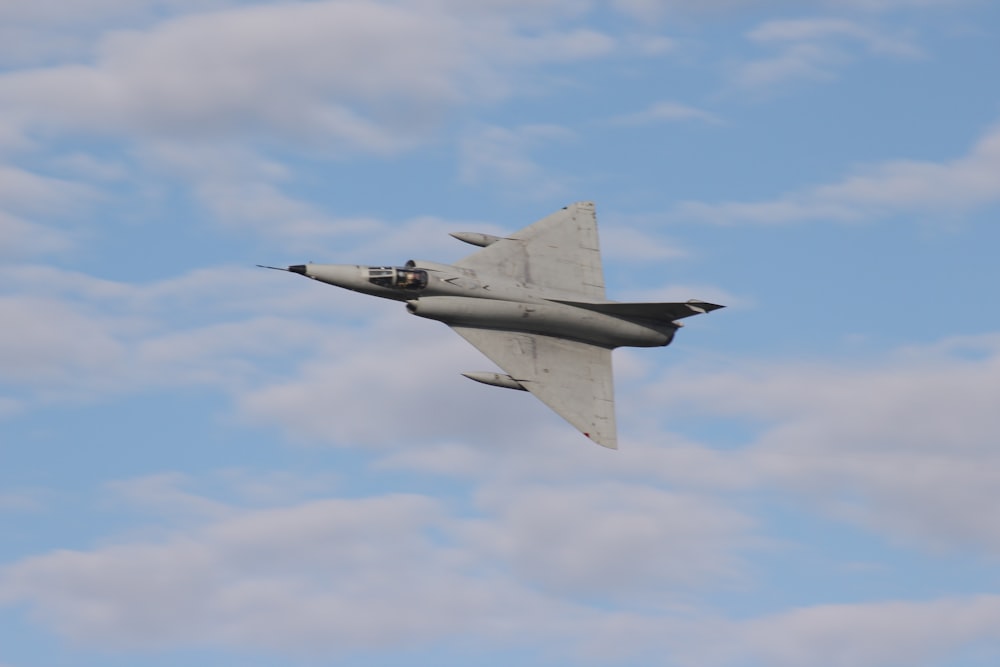 a fighter jet flying through a cloudy blue sky