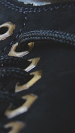 Close-up of black fabric with metallic eyelets threaded with a black cord, showcasing detailed stitching and texture.