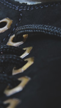 Close-up of black fabric with metallic eyelets threaded with a black cord, showcasing detailed stitching and texture.