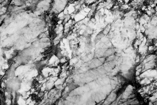 A close-up view of a marble surface with a complex pattern of veins and textures. The image showcases a mixture of light and dark areas, with intricate lines and swirls throughout.