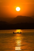 the sun is setting over the water with a boat in the foreground