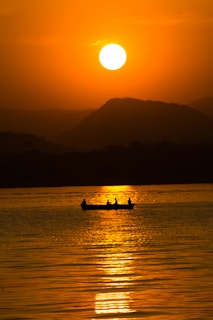 the sun is setting over the water with a boat in the foreground