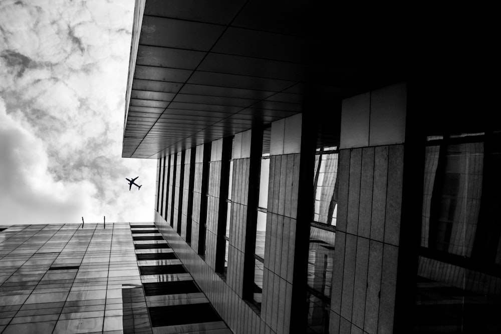 a black and white photo of a plane flying over a building