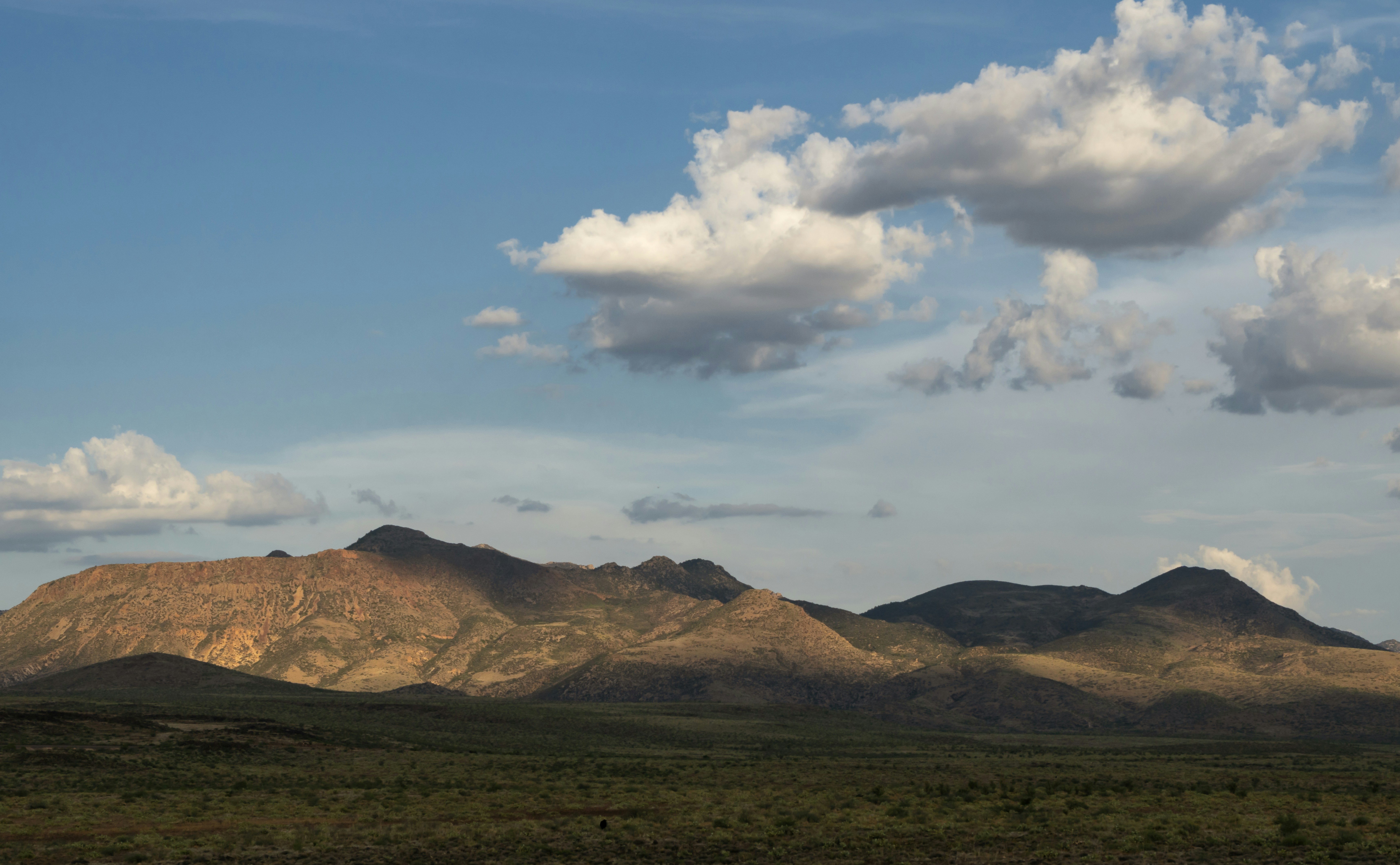 a mountain range with a few clouds in the sky, With the help of a setting sun, cumulus clouds cast shadows on the northern edge of the Weaver Mountains.