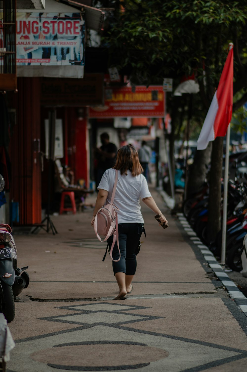 a woman walking down a sidewalk carrying a pink backpack