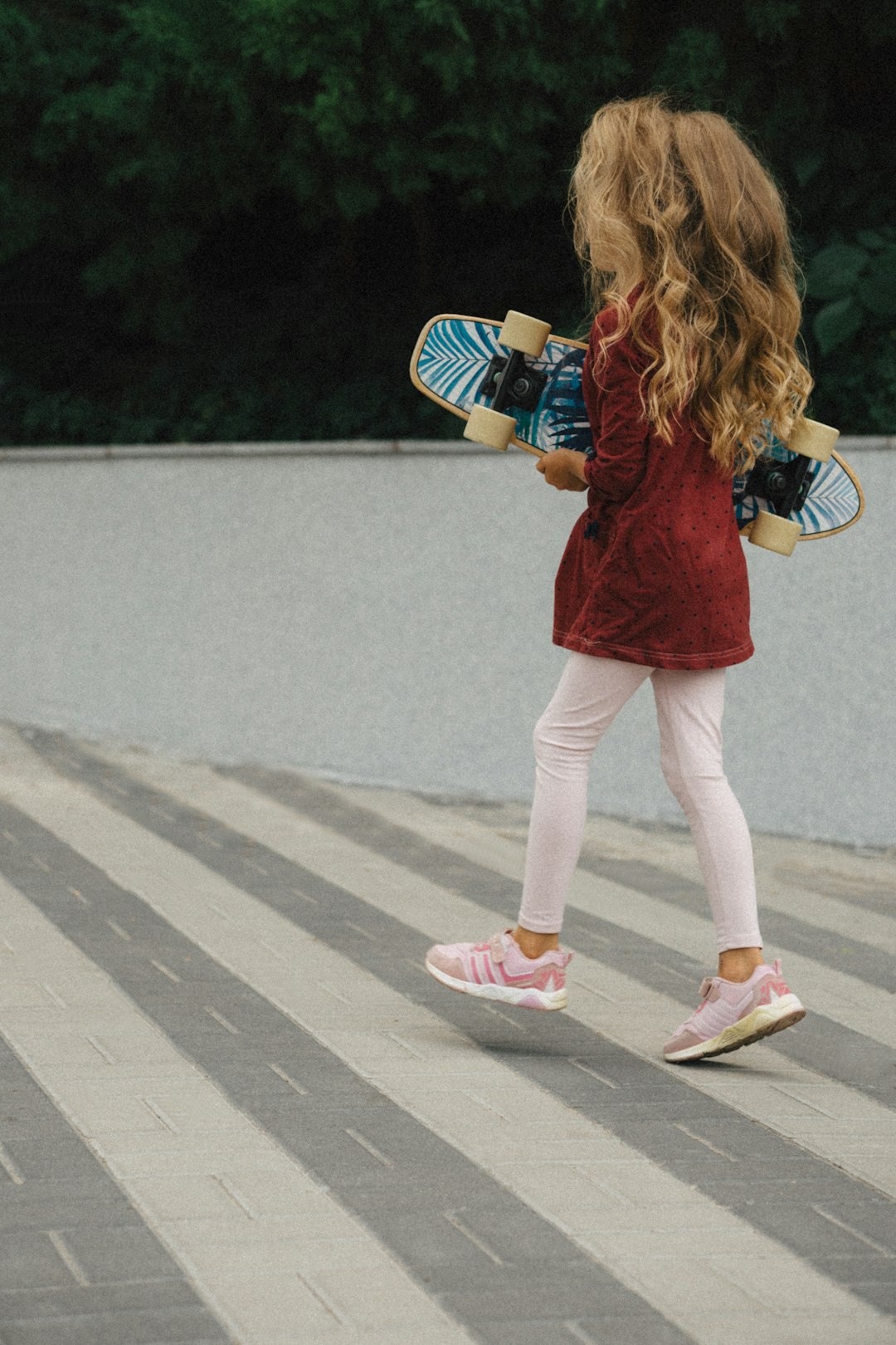 a little girl holding a skateboard and wearing pink shoes