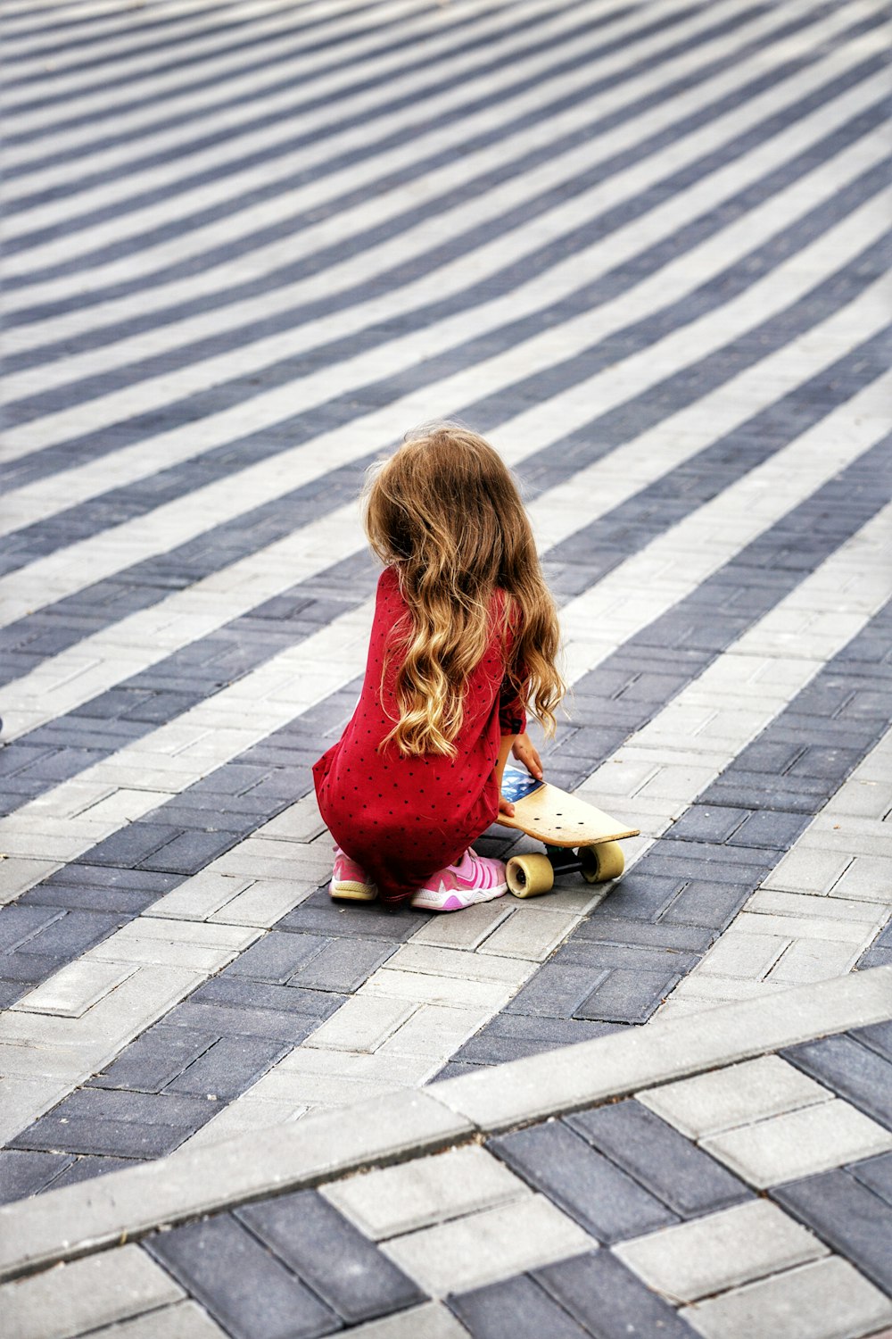 una bambina seduta a terra con uno skateboard