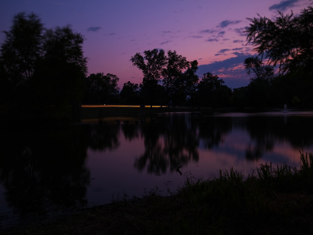 um lago com um céu roxo e árvores ao fundo