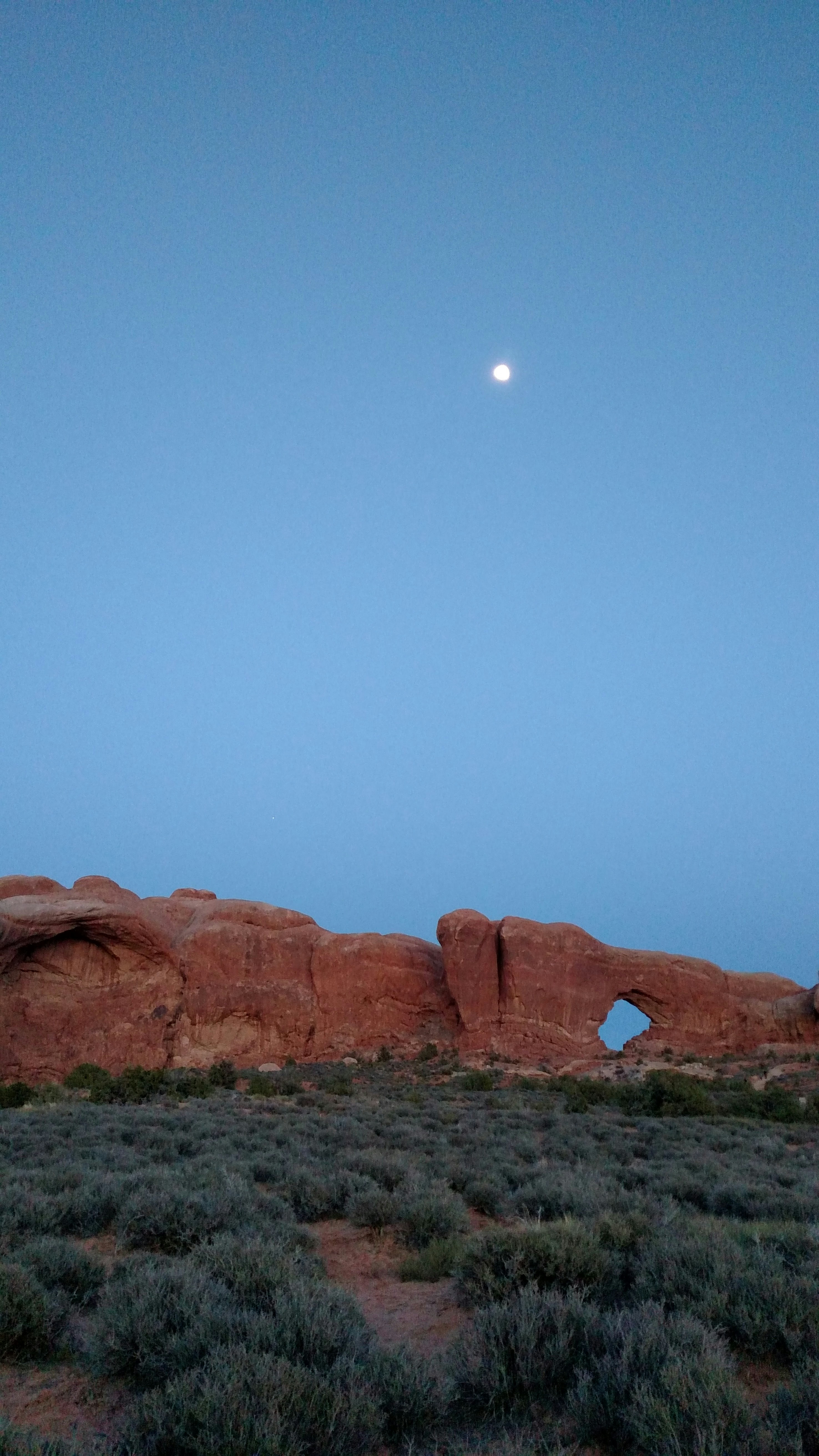 the moon is setting over a rock formation