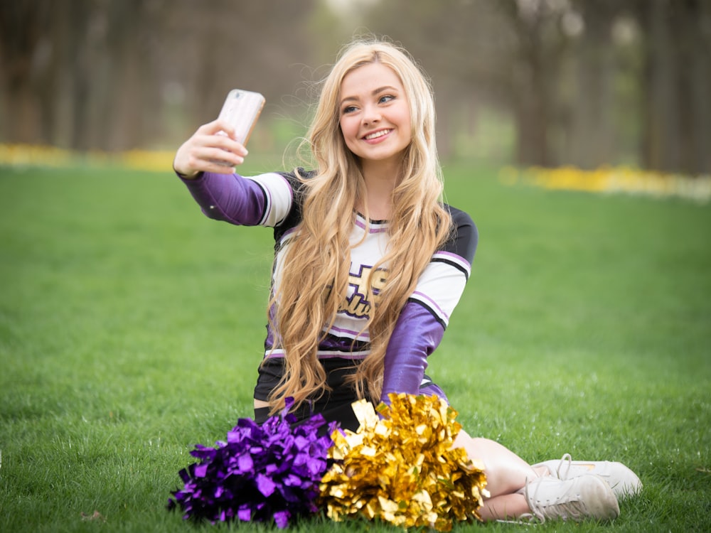 a girl sitting on the grass taking a selfie with her cell phone