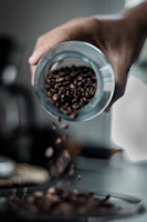 Artisan hands delicately pouring rare coffee beans into a glass jar under soft, moody lighting.