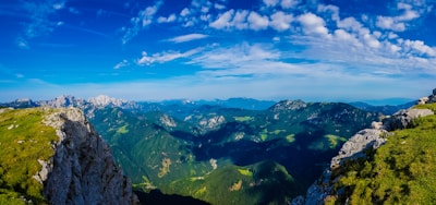 A panoramic shot of the Jura mountains under a clear blue sky, dotted with lush green forests.