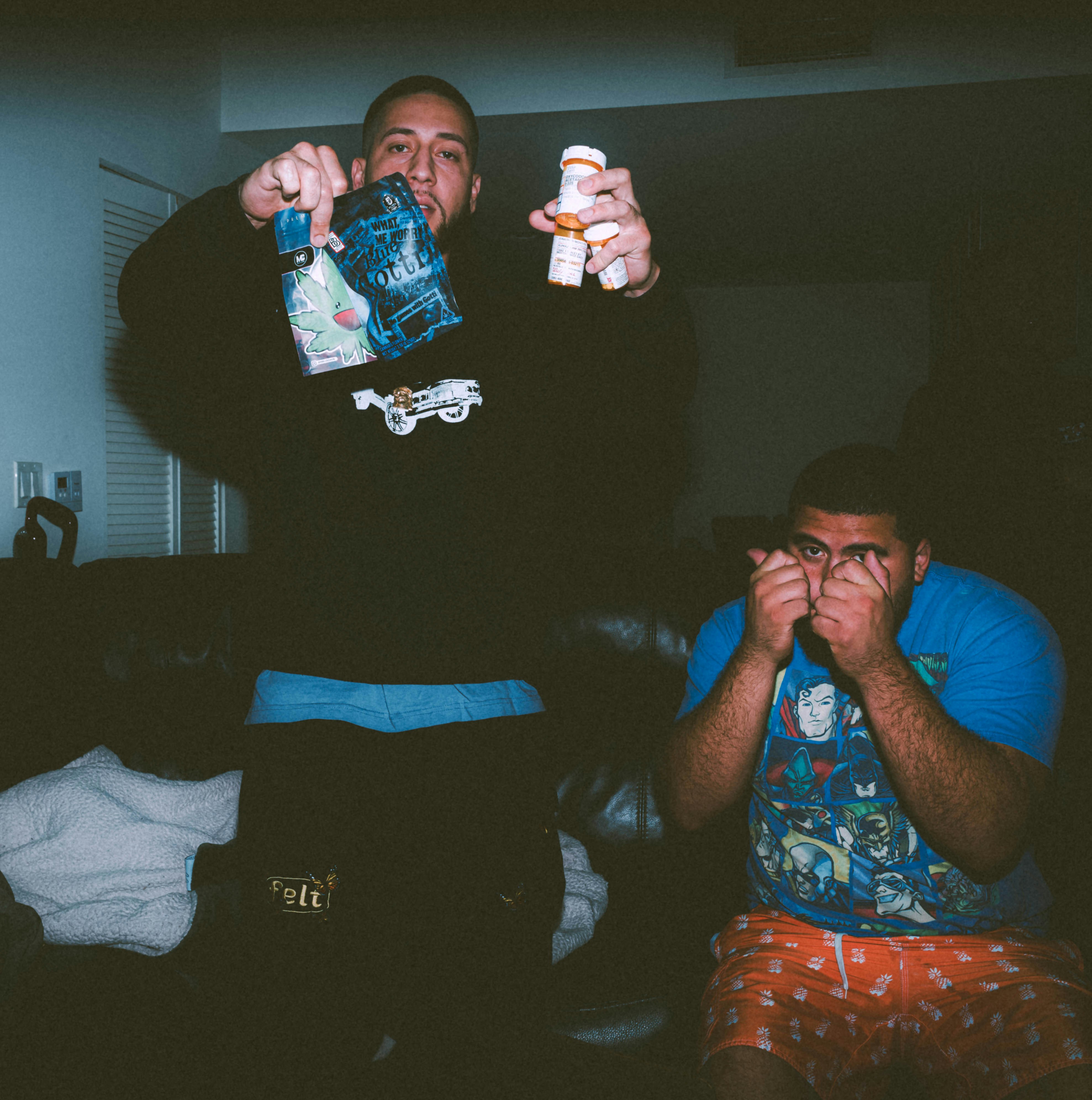 two men sitting on a couch while one holds a bottle and the other holds a