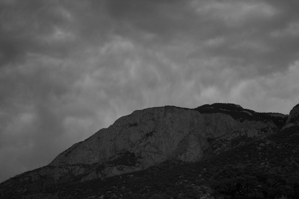 a black and white photo of a mountain under a cloudy sky