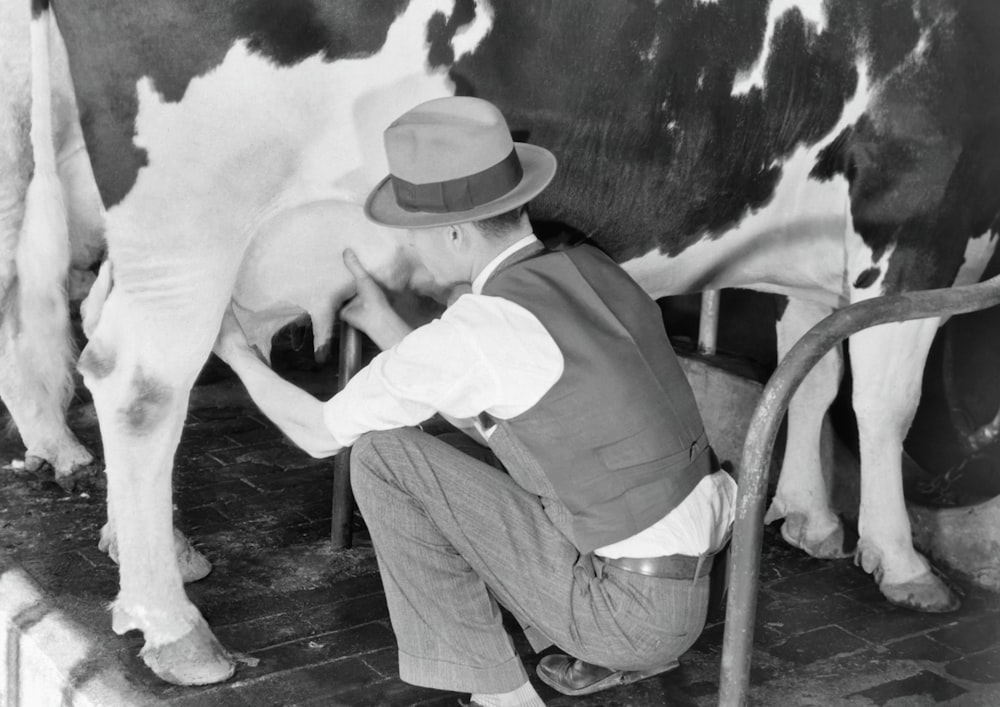 a man is milking a cow in a black and white photo