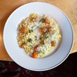 Close-up of creamy polenta served in a rustic jar topped with melted cheese and fresh herbs.
