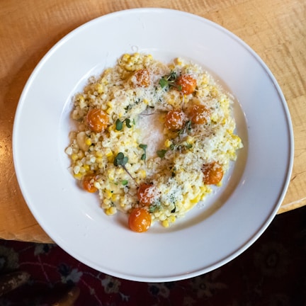 Close-up of creamy polenta served in a rustic jar topped with melted cheese and fresh herbs.