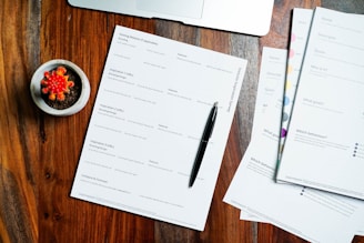 a wooden table topped with papers and a pen