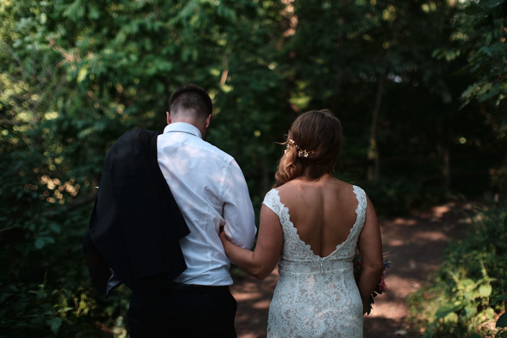 a bride and groom walking down a path in the woods