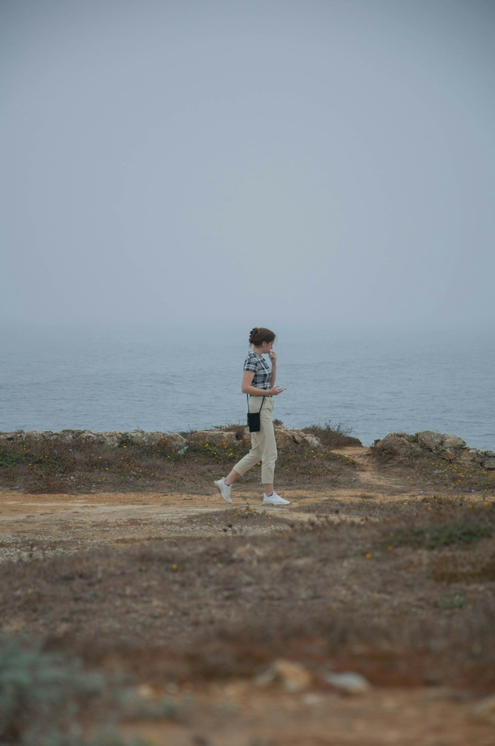 a man walking across a dirt field next to the ocean