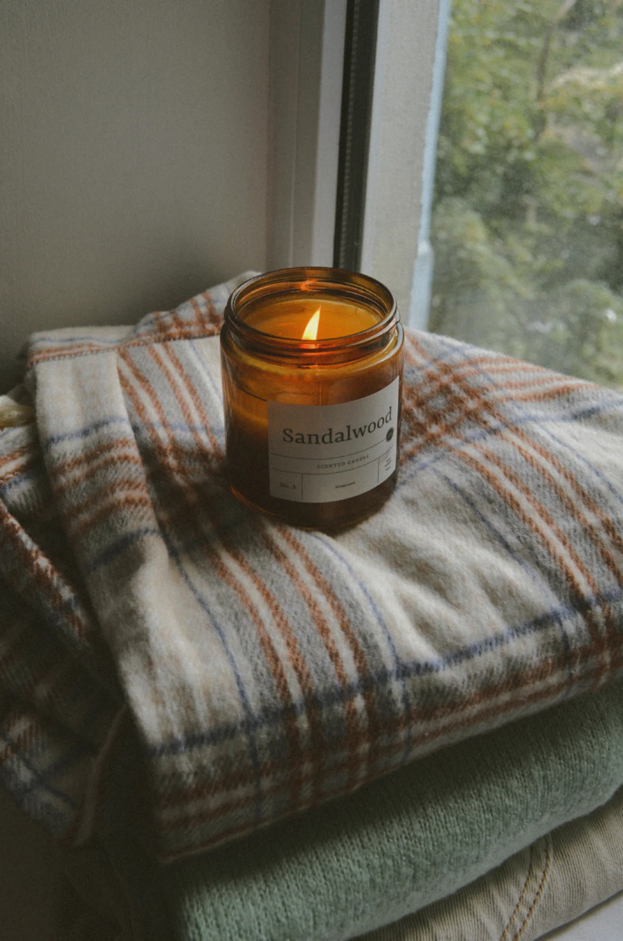 A candle on a blanket beside a window