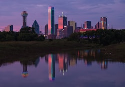 a city skyline is reflected in the still water of a pond