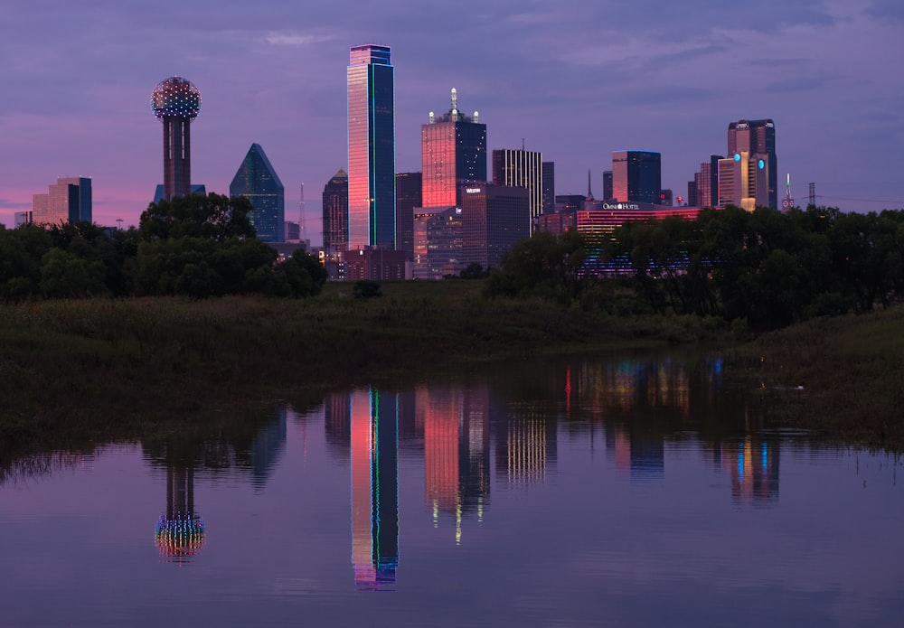 a city skyline is reflected in the still water of a pond
