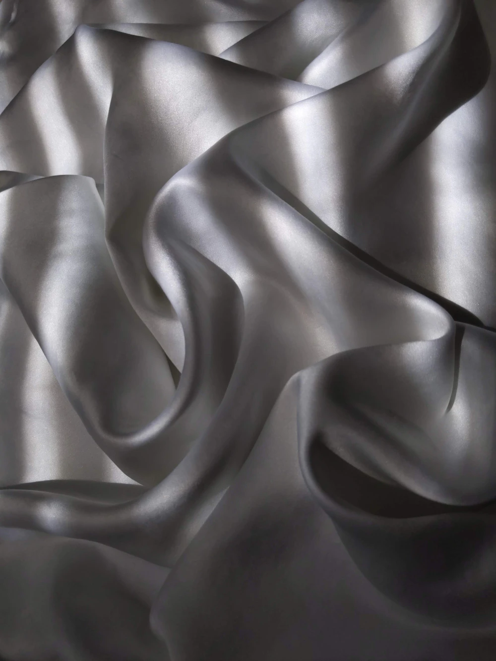 Pewter silk twisting in slow ribbons across a dimly lit studio surface
