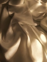 A silk sleepwear strap slipping off a shoulder, light catching the fabric's subtle shimmer against a dark background.