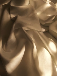 A silk sleepwear strap slipping off a shoulder, light catching the fabric's subtle shimmer against a dark background.