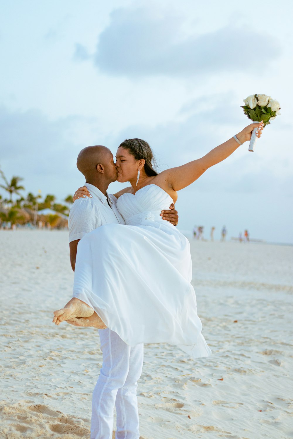 a bride and groom kissing on the beach