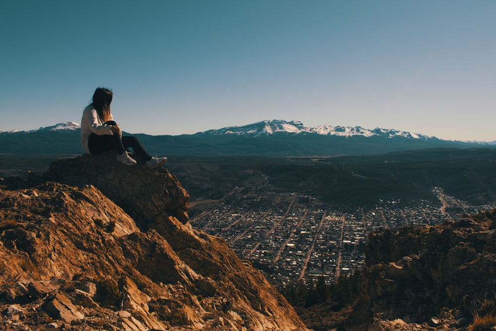 a woman sitting on top of a mountain overlooking a city