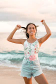 A joyful woman walking on a beach boardwalk wearing floral print shorts and a light tank top