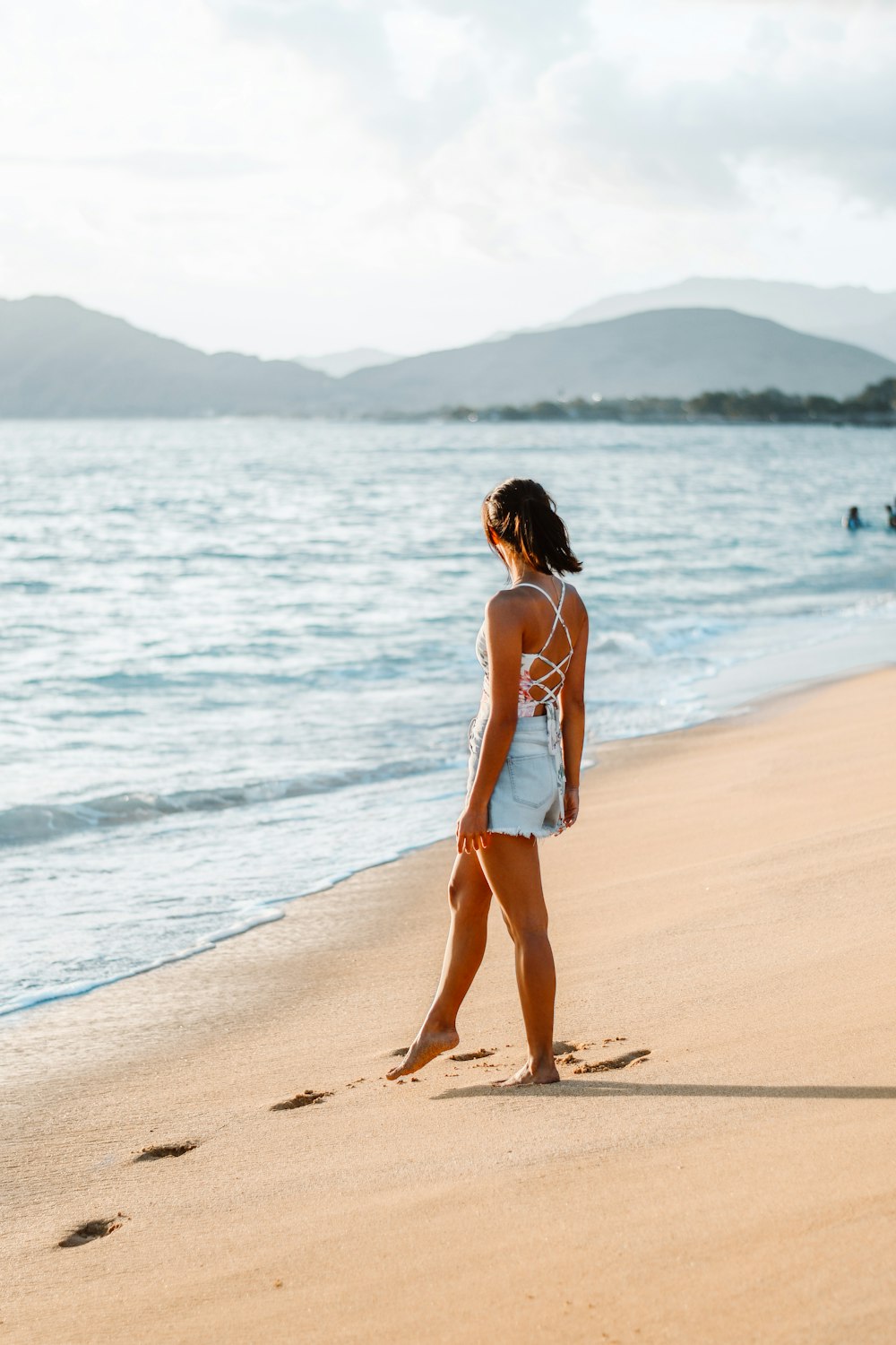 a woman standing on top of a sandy beach next to the ocean