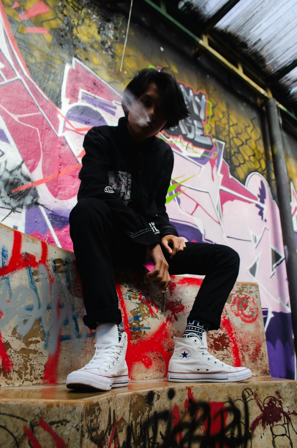 a young man sitting on top of a graffiti covered wall