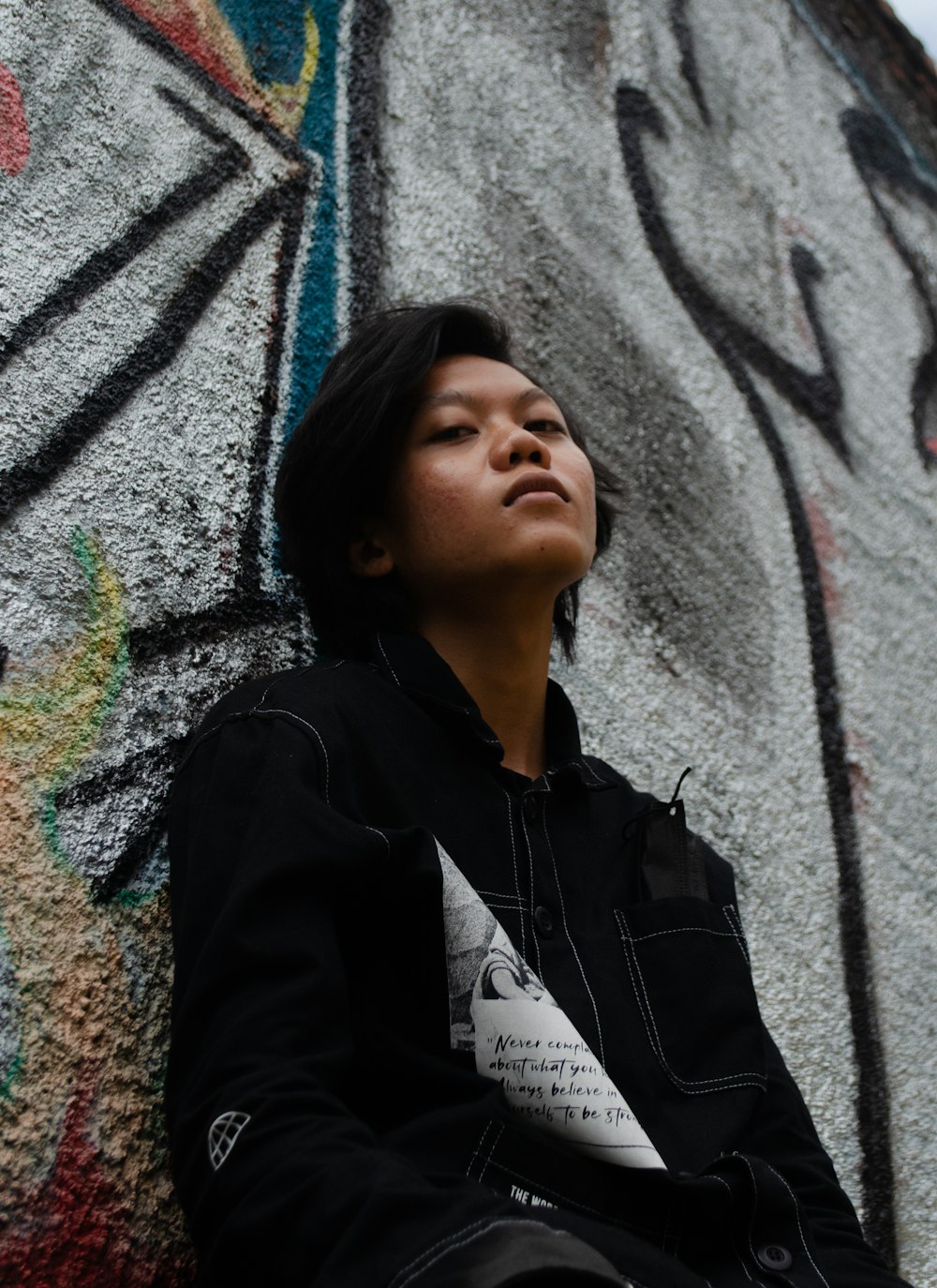 a woman sitting against a wall with graffiti on it