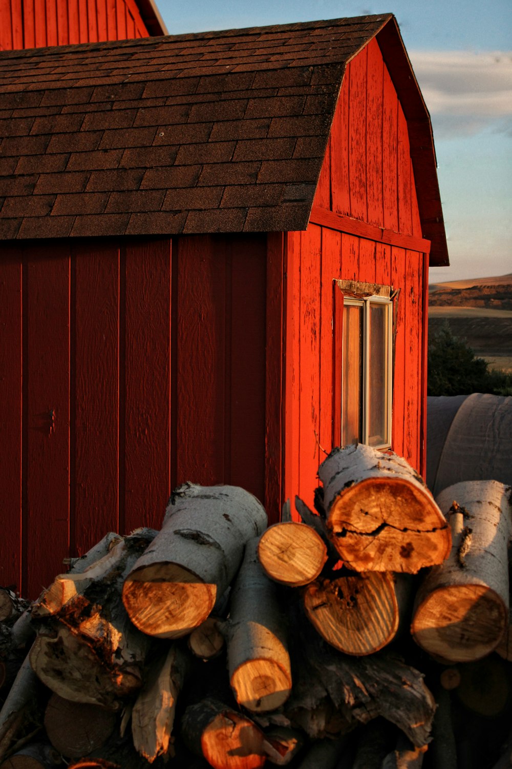 a pile of logs in front of a red barn
