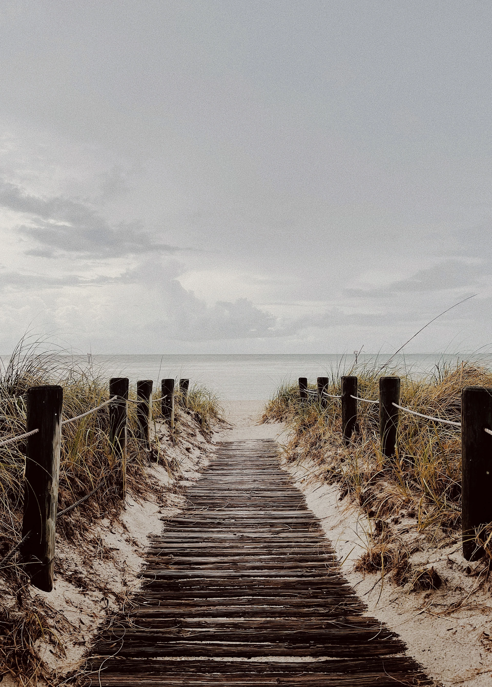 a wooden path leading to the beach on a cloudy day
