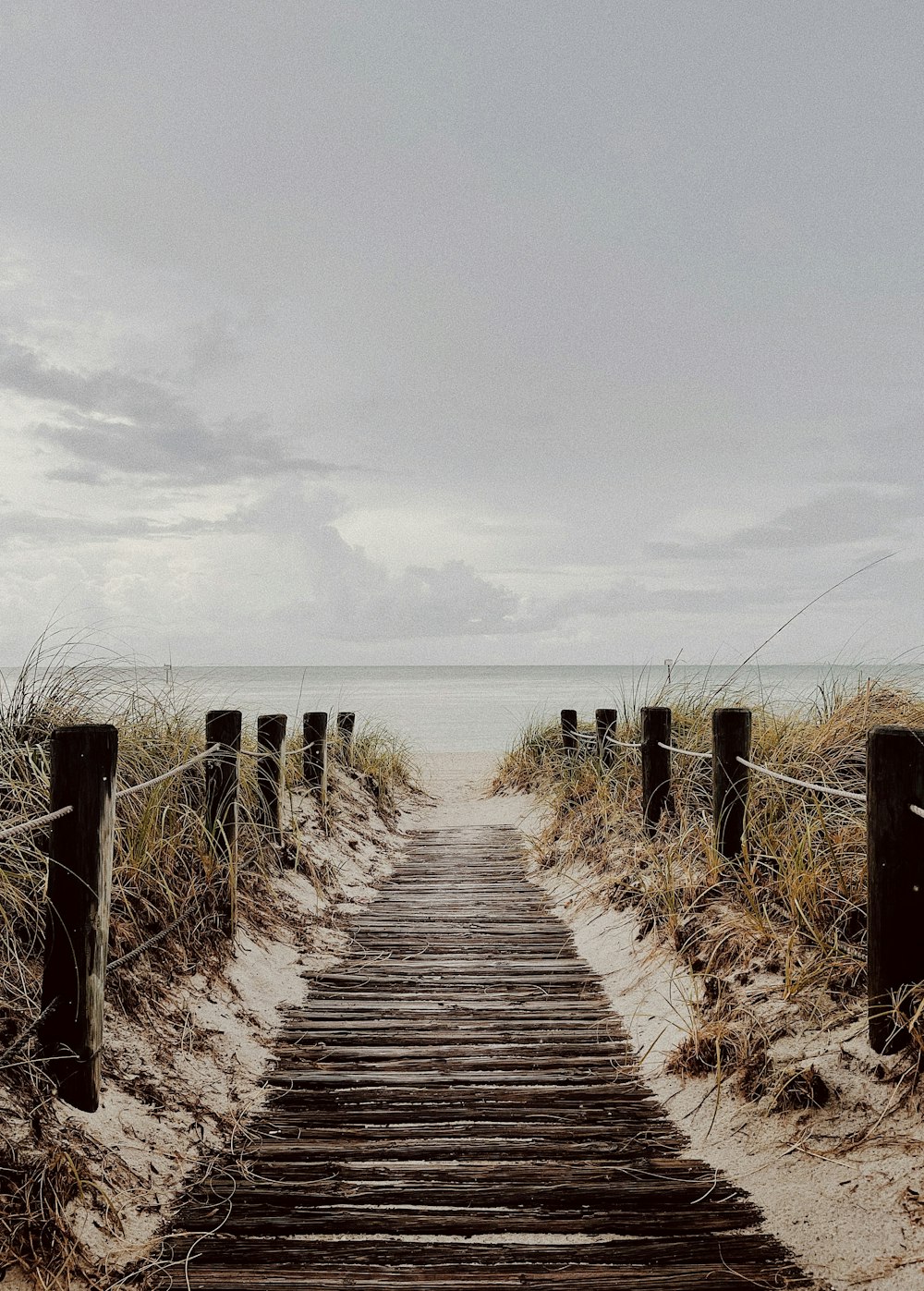 a wooden path leading to the beach on a cloudy day
