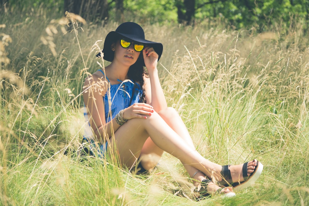 a woman wearing a hat and sunglasses sitting in a field