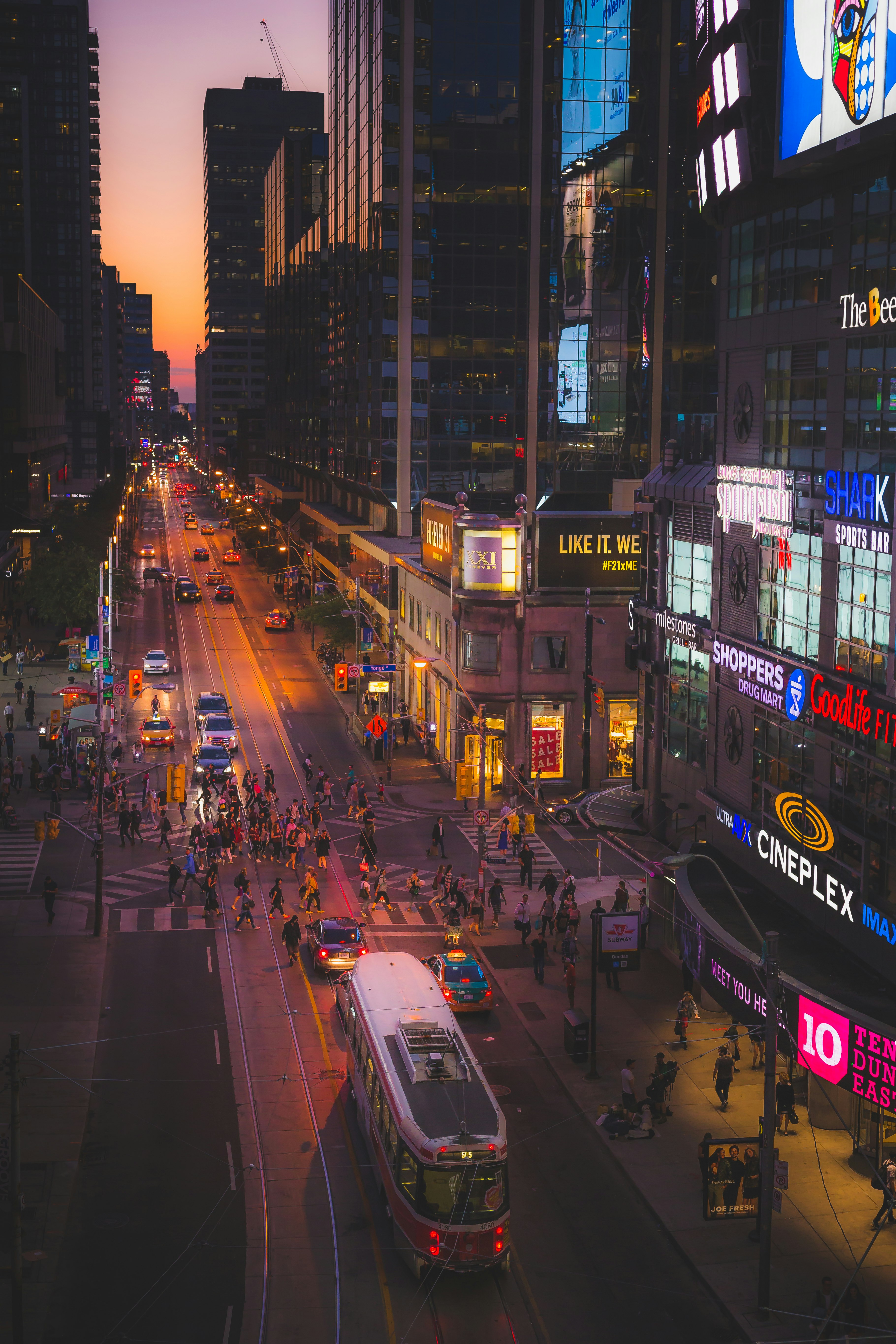 City boulevard at dusk with illuminated street lamps, car light trails, and glowing building windows stretching into the distance