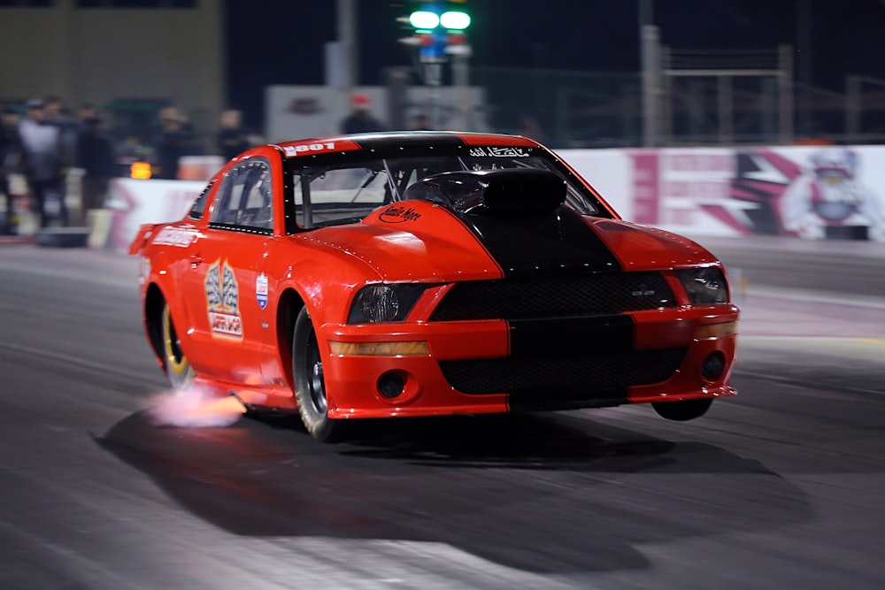 a red car driving down a race track at night