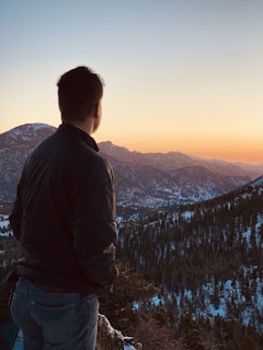 A traveler standing on a mountain peak overlooking a vast landscape at sunset.