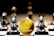A gold Ethereum token is prominently placed on a black and white chessboard surrounded by several metallic chess pieces. The focus is on the Ethereum symbol on the coin, while the chess pieces appear slightly out of focus in the background. The lighting emphasizes the reflective surfaces of both the coin and the chess pieces.