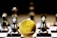 A gold Ethereum token is prominently placed on a black and white chessboard surrounded by several metallic chess pieces. The focus is on the Ethereum symbol on the coin, while the chess pieces appear slightly out of focus in the background. The lighting emphasizes the reflective surfaces of both the coin and the chess pieces.